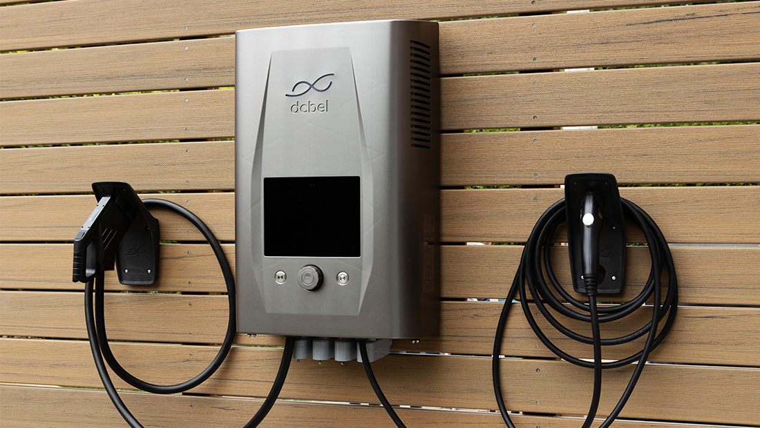 Close-up of the dcbel Ara Home Energy Station mounted on a wooden wall, showing dual charging cables designed for smart EV and home energy management.