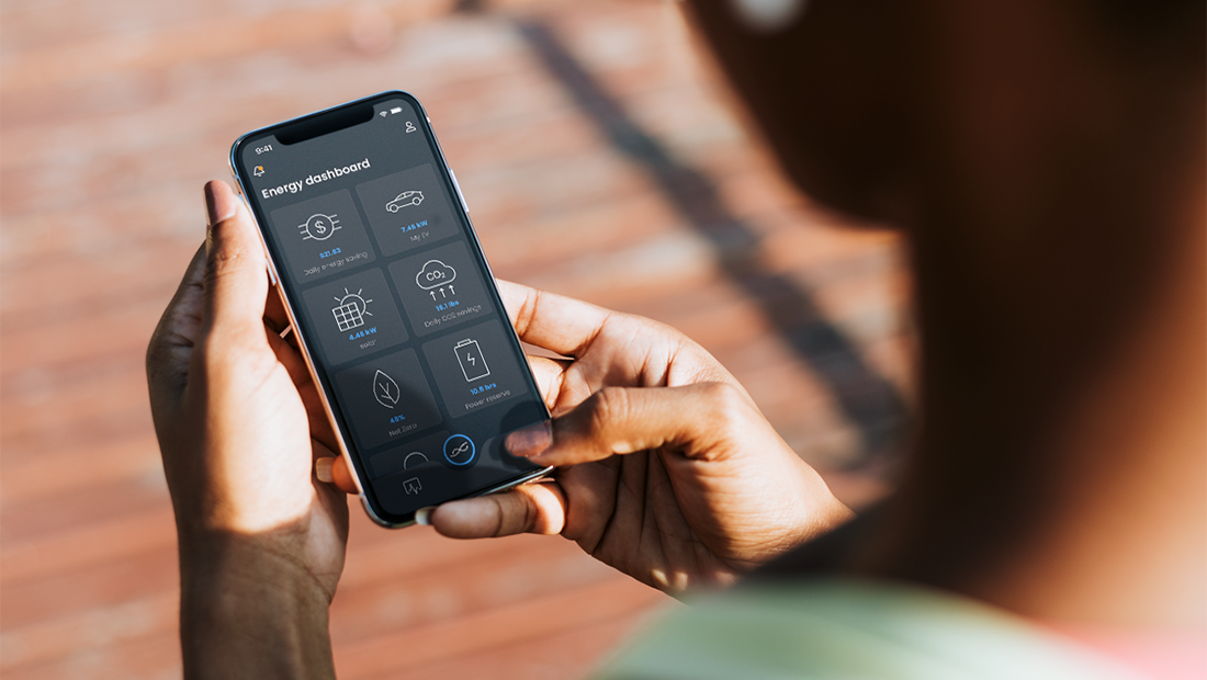 A person holds a smartphone showing an energy dashboard app with metrics like daily savings, EV power usage, solar energy production, CO2 reduction, and net zero status, highlighting smart home integration and intelligent energy optimization for eco-conscious users.