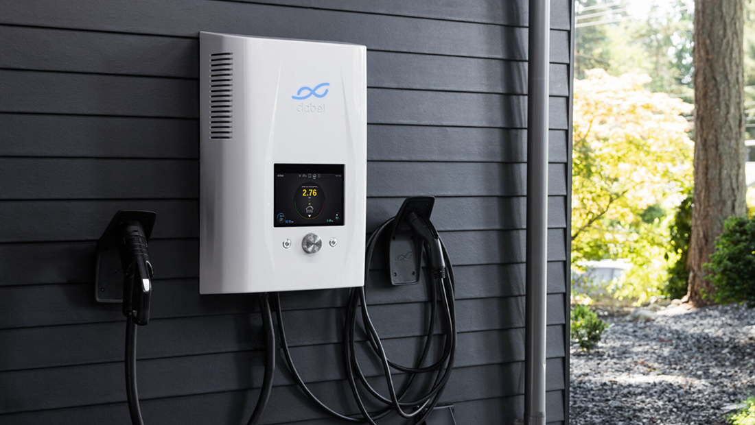 A smart energy device for electric vehicles is mounted on a wall outdoors, surrounded by greenery. The energy management system features a digital display and dual charging cables, enabling real-time energy monitoring and personalised energy management. This connected smart device supports home efficiency through seamless automation and integration with other smart energy devices.