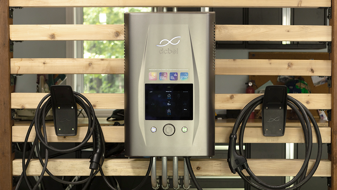 A dcbel Home Energy Station mounted on a wooden slatted wall, with two charging cables coiled on either side of the unit.